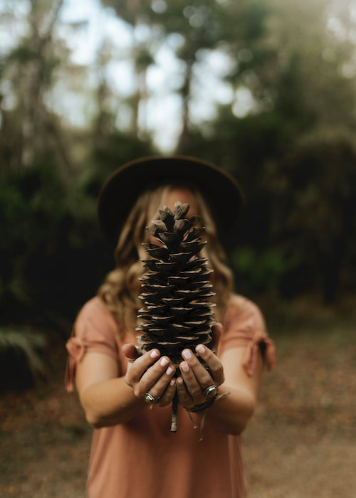 Kelly Bruce, forest therapy guide and virtual forest bathing guide, holding a pinecone 